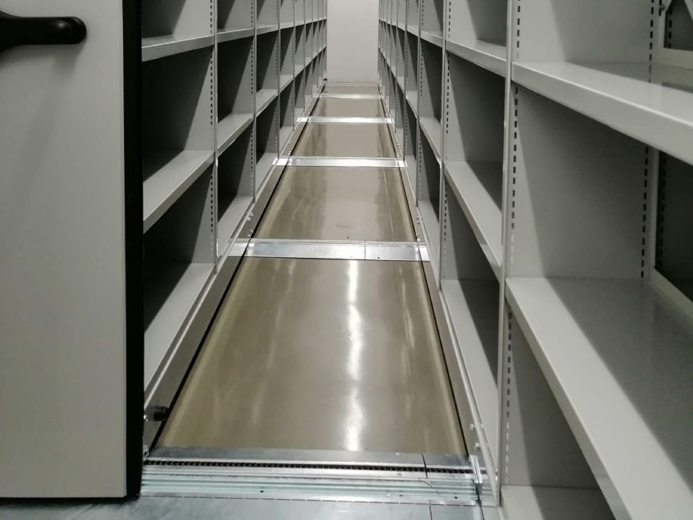 Corredor entre estantes compactas, com os carris no pavimento, no Arquivo Alto da Eira