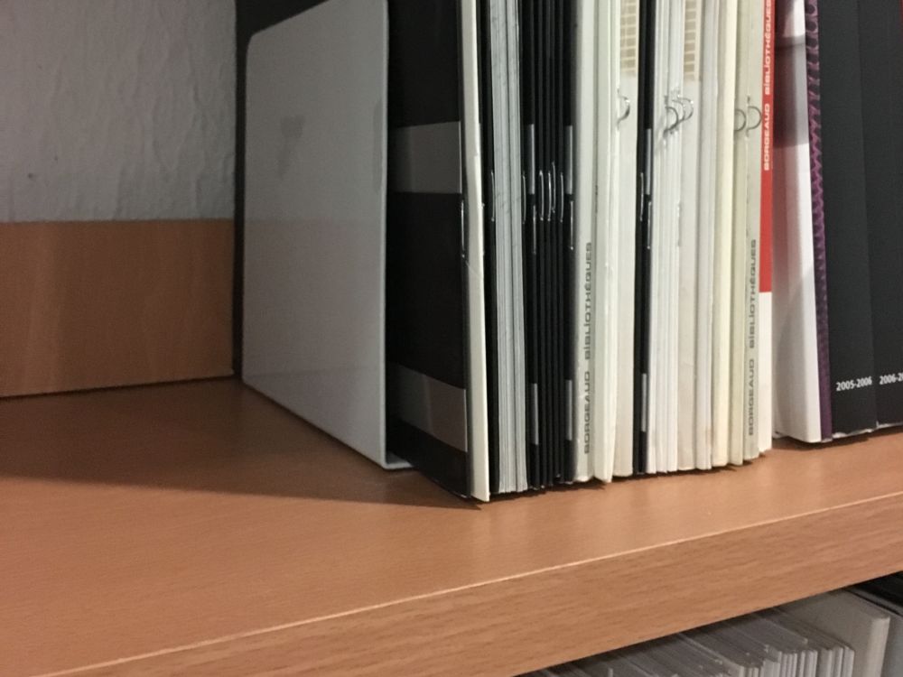 Aparador de livros metálico branco a segurar revistas numa estante